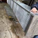Technician handling large industrial heat exchanger during repair at St. Louis radiator shop