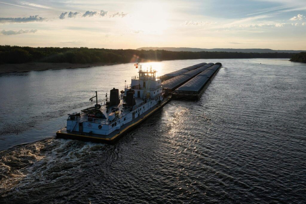 Towboat pushing covered barges on a river at sunset, illustrating marine cooling solutions in action.